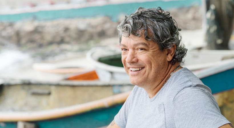 Smilende mann på stranden med båter på land i bakrgrunnen